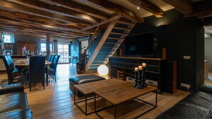 Un'ampia zona giorno con soffitto in legno, una scala, un'area pranzo e un angolo salotto con tavolino.