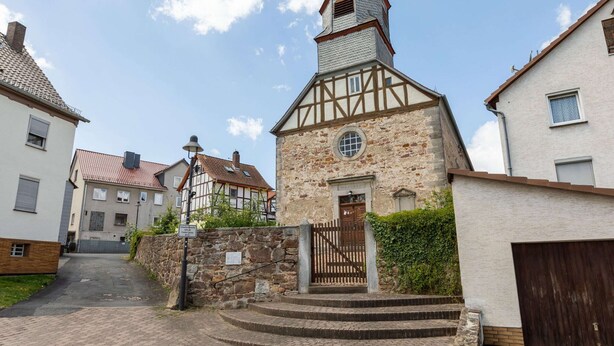 Un edificio tradicional con entramado de madera y fachada de piedra, una puerta de madera y una pequeña ventana circular.