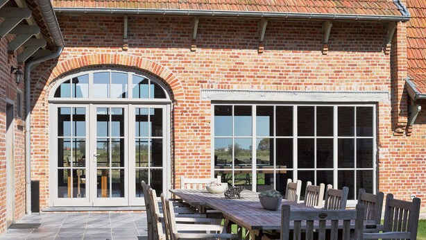 A brick building with large windows and a patio area with wooden furniture. - Diksmuide Mansion With Games (Diksmuide)