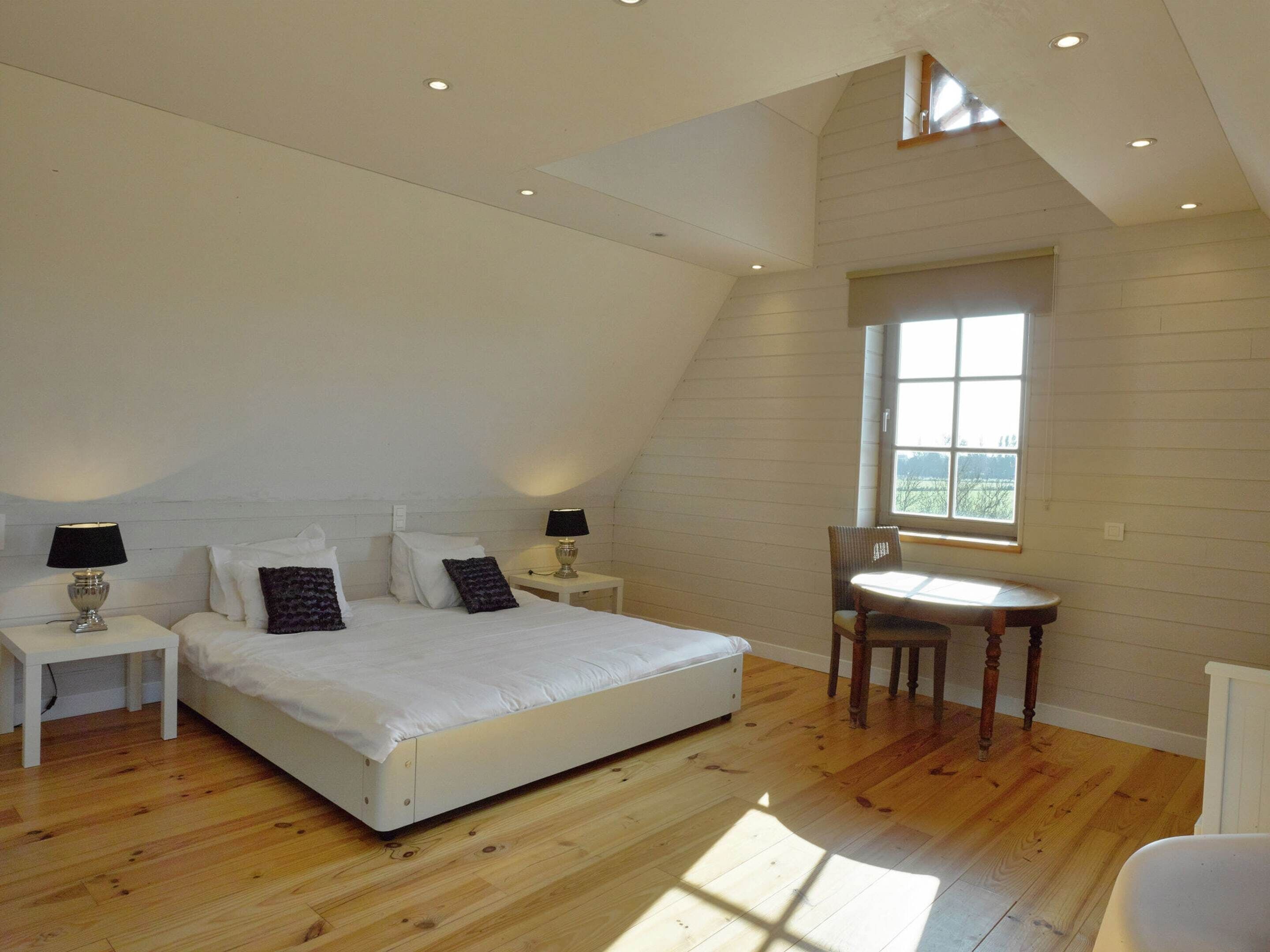 A bedroom with a large bed, two bedside tables, a chair, and a window.