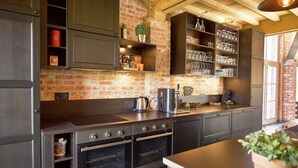 A kitchen with brick walls, dark cabinetry, and a coffee machine. - Diksmuide Mansion With Games (Diksmuide)