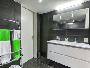 Une salle de bain moderne avec des carreaux foncés, un porte-serviettes chromé, un lavabo blanc et un miroir au-dessus du lavabo.