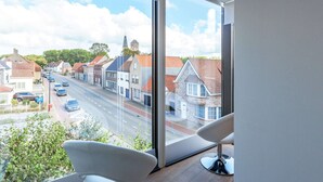 A modern room with large windows offering a view of a street lined with traditional houses and a church steeple.