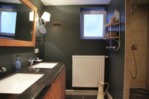 Ein Badezimmer mit zwei Waschbecken, einem Spiegel, einem Handtuchhalter, einem Heizkörper und einer Dusche.