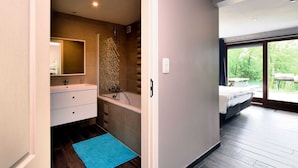 A modern bathroom with a shower, a sink, and a mirror. There is a blue rug on the floor, and a window with a view of greenery outside. - Luxurious Chalet in Beauraing With Sauna (Beauraing)