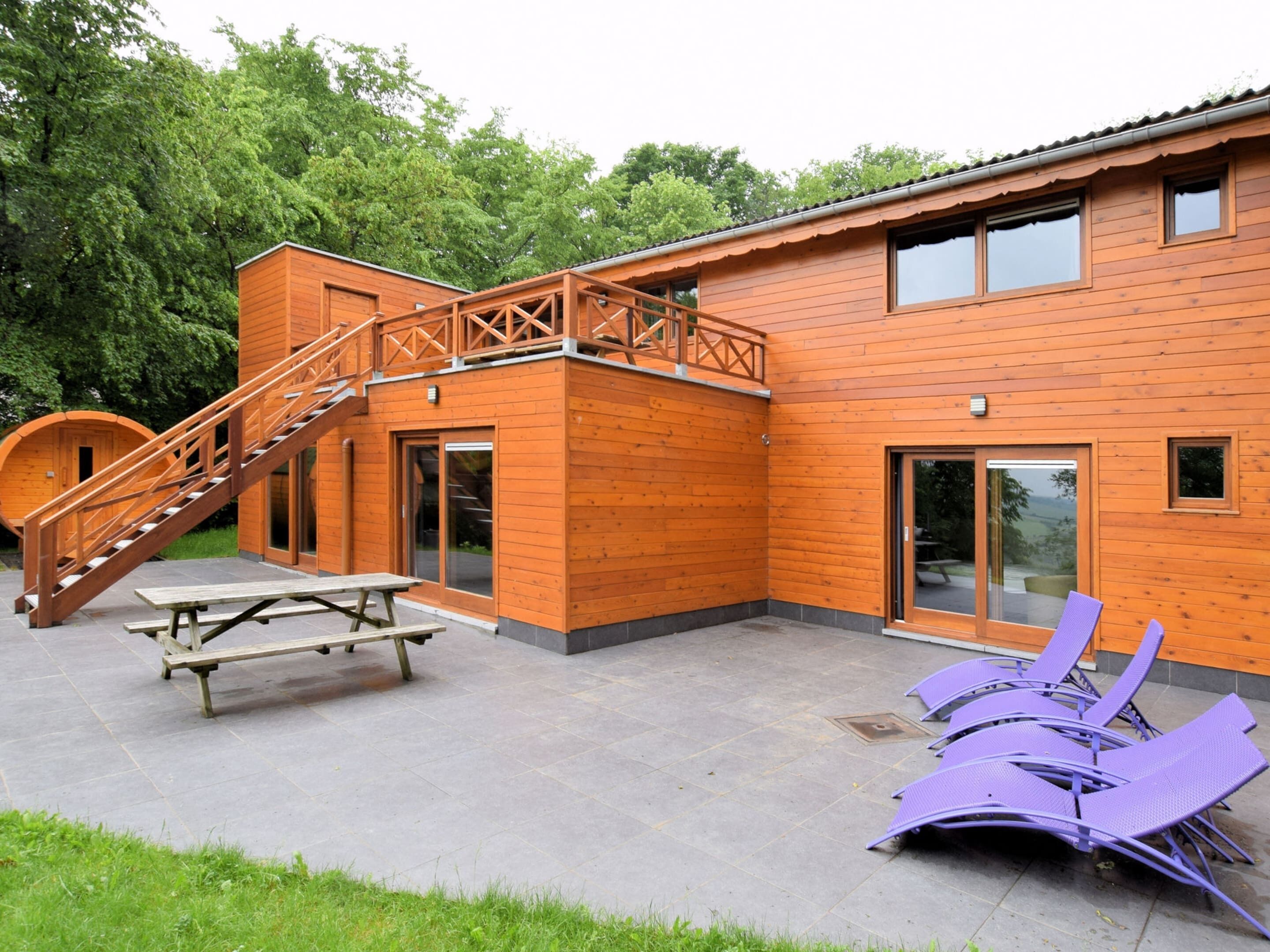 Un bâtiment en bois avec un escalier, une table de pique-nique et des chaises violettes.