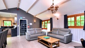 A modern living room with grey sofas, a wooden coffee table, and a chandelier. There is a kitchen area visible in the background. - Luxurious Chalet in Beauraing With Sauna (Beauraing)