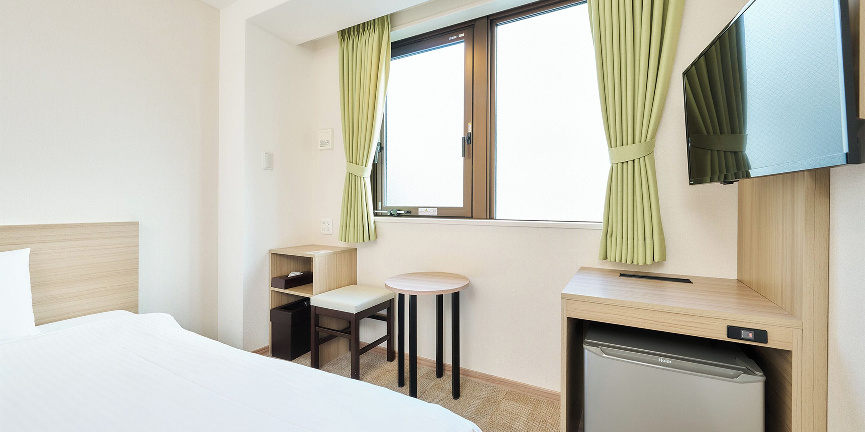 Ett hotellrum med en säng, ett skrivbord med en stol, ett litet bord, en tv och ett litet kylskåp.
