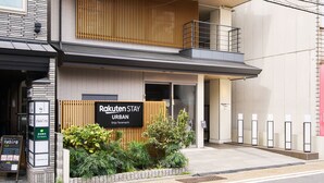 A modern building with a sign for 'Rakuten Stay URBAN' and a small garden area in front. - Rakuten STAY URBAN Shijo Teramachi (Kyoto)