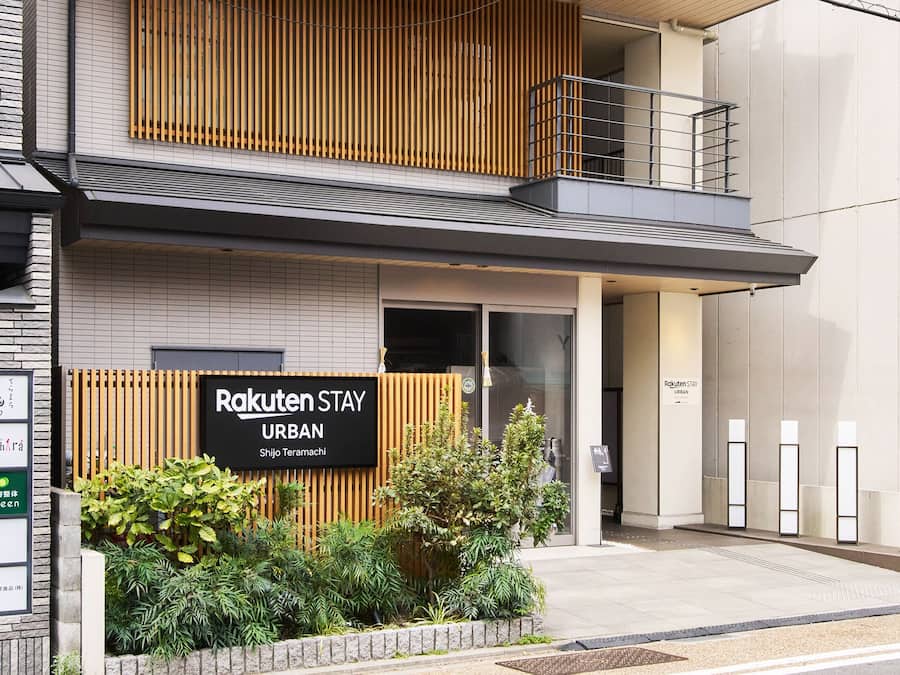 Un edificio moderno con un cartel que dice 'Rakuten Stay URBAN' y un pequeño jardín delantero.
