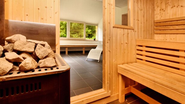 Sala de sauna com bancos de madeira, um banco fora da sauna e uma pilha de pedras.
