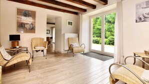 Quarto amplo com assoalho de madeira, móveis de vime e grandes janelas com vista para o verde.