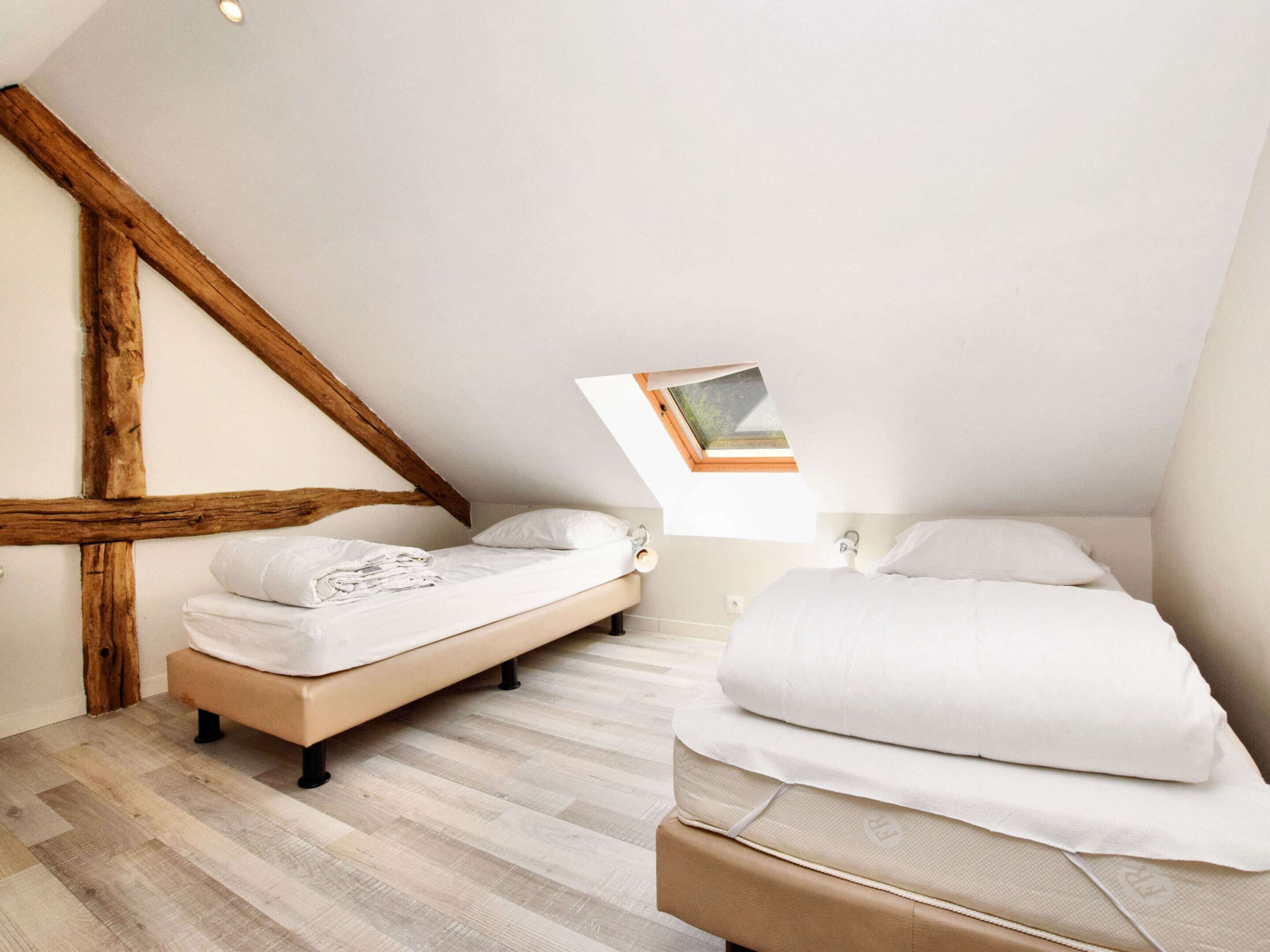 A bedroom with a sloped ceiling, wooden beams, a skylight, and a bed with white bedding.