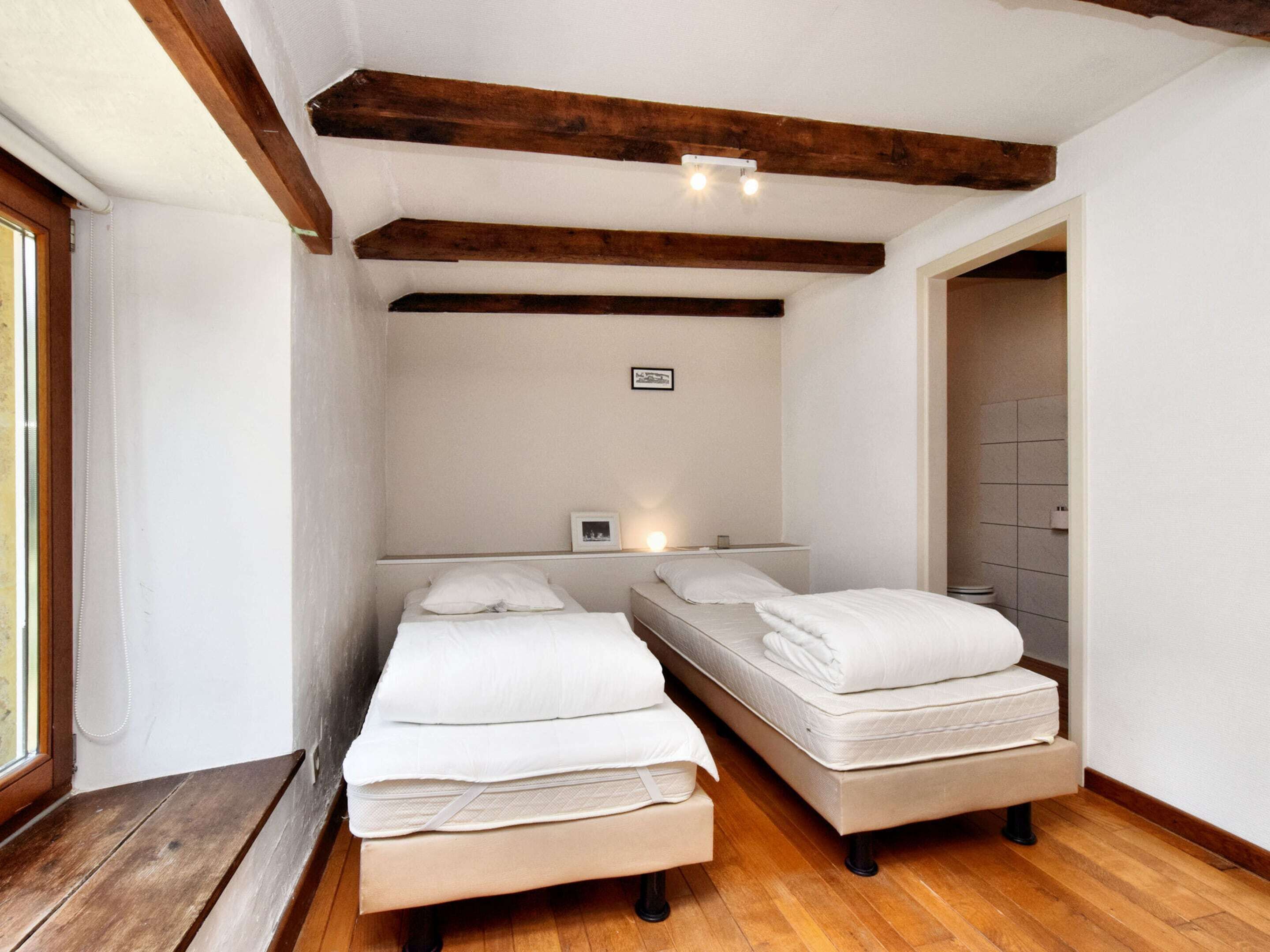 A room with two beds, wooden beams on the ceiling, a small table, and a window.