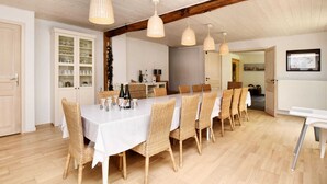 Uma sala de jantar com uma mesa comprida, cadeiras de vime e luminárias pendentes.