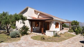 Ein eingeschossiges Haus mit Terrasse, Satellitenschüssel und Blick auf die Berge.