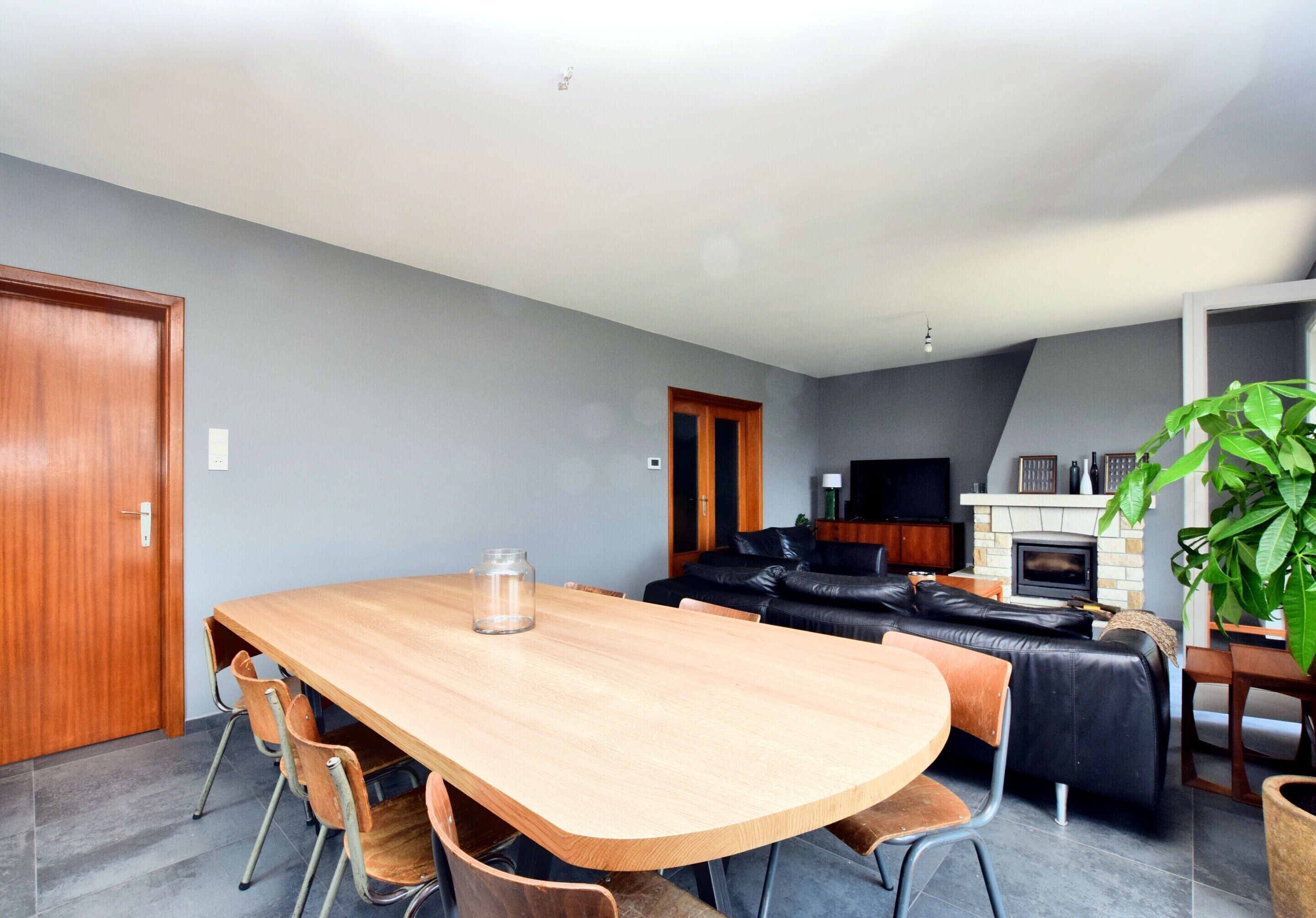 A modern living room with a wooden dining table, black leather sofa, and a fireplace.