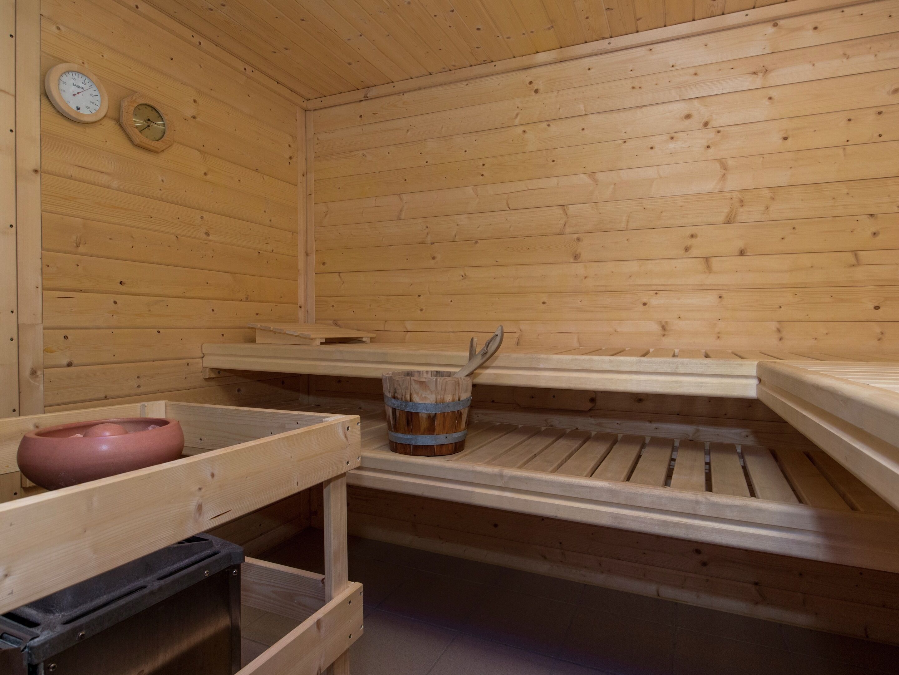 Un sauna en bois avec des bancs, un seau en bois et deux horloges murales.