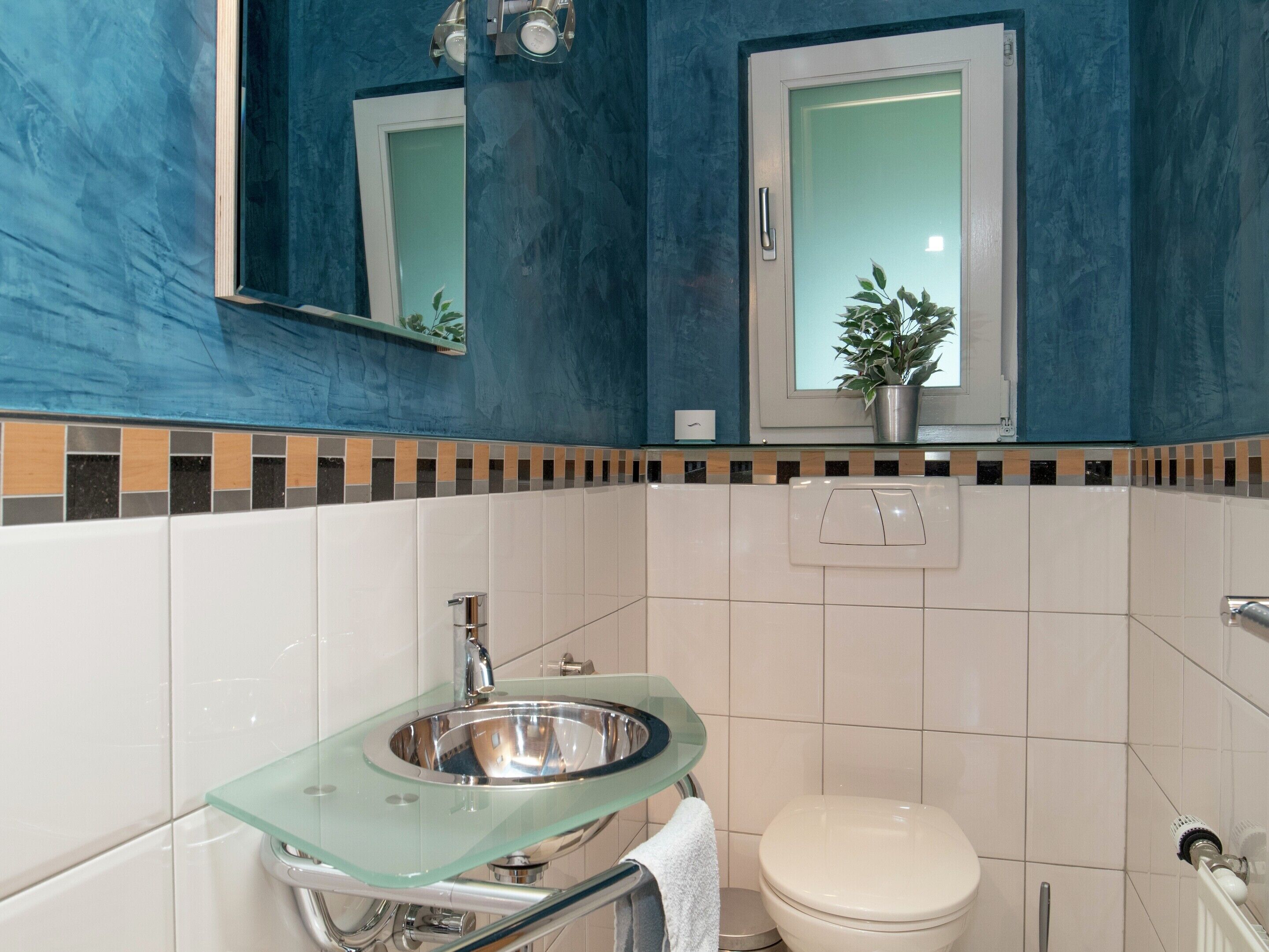 A bathroom with a glass sink, white toilet, and a blue wall with a decorative tile border.