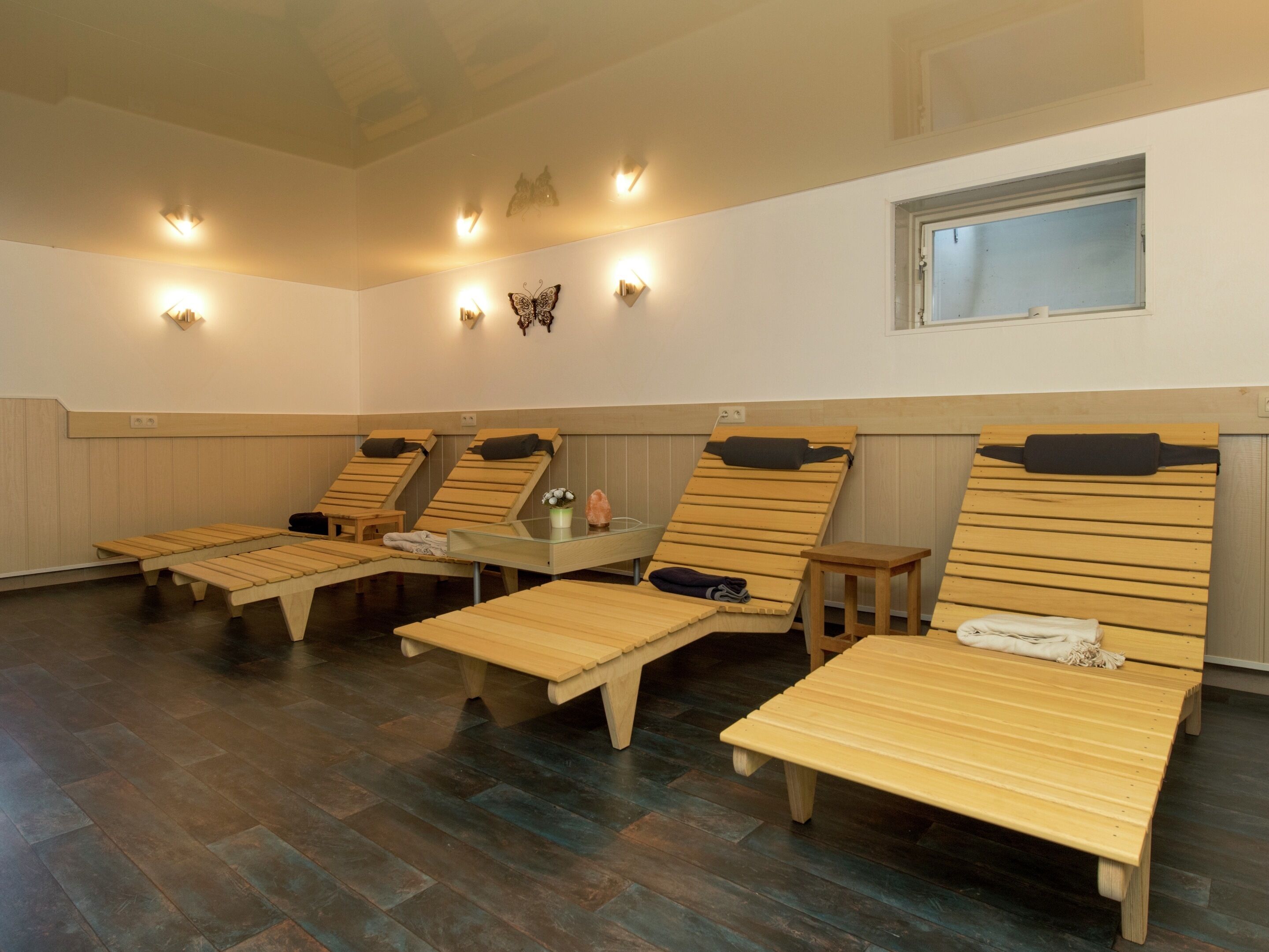 Una sala de sauna con camastros de madera, una mesa de vidrio y luces en la pared.