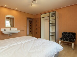 A bedroom with a bed, a bedside table with a mirror, a wardrobe, and a chair.