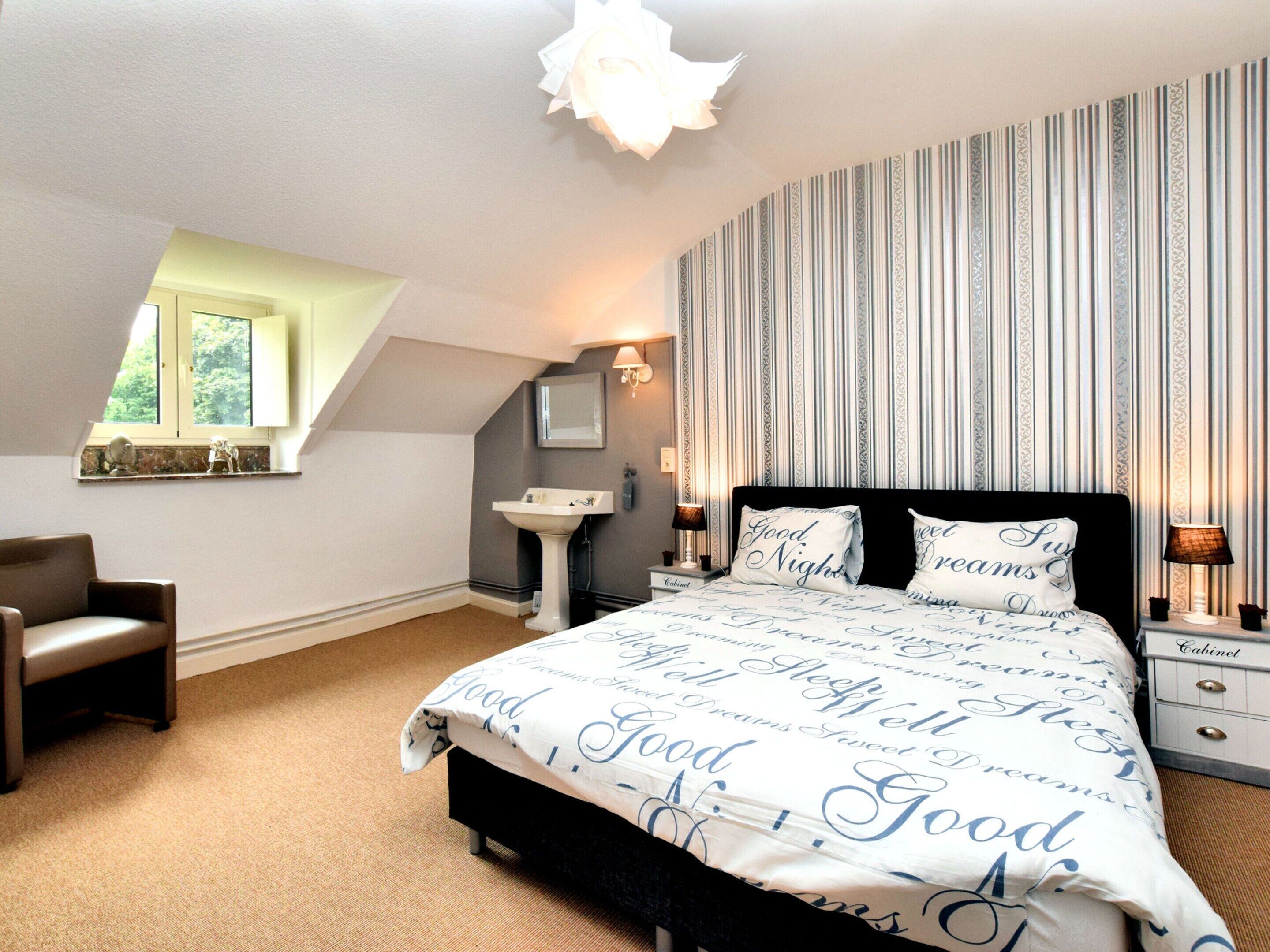A bedroom with a bed, a nightstand, a chair, a window, and a wall with vertical stripes.