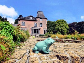 Un chemin de pierres mène à une grande maison rose surmontée d’une tourelle.