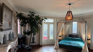 A bedroom with a four-poster bed, a large potted plant, a fireplace, and a view through a glass door. - Magnificent Luxury Chateau in Vast Garden with Sauna & Hot Tubs (Chiny)