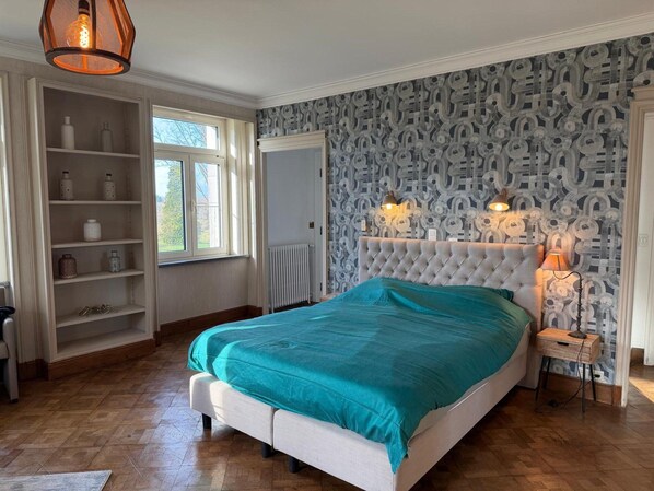 A bedroom with a large bed, built-in shelving, a radiator, and a patterned wallpaper.