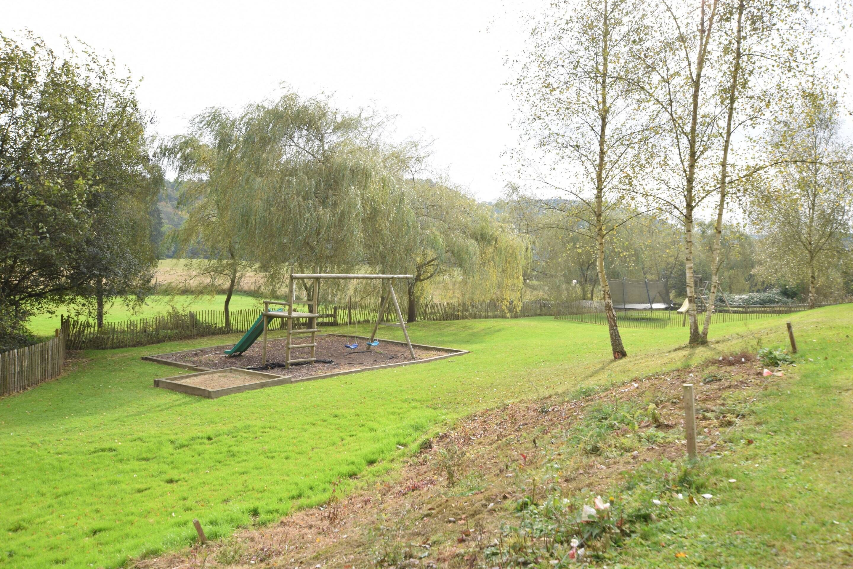 A playground with a swing set and slide, surrounded by grass and trees.
