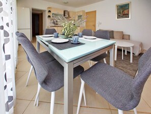 Un comedor con una mesa de vidrio, sillas tapizadas de gris y un florero con flores.