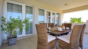 Ein Balkon mit Korbmöbeln, einem Tisch gedeckt mit Tellern, Schüsseln und einem Obstkorb.