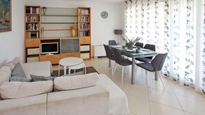 Ein modernes Wohnzimmer mit Sofa, Esstisch mit Stühlen, Fernseher und Bücherregalen.