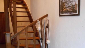 A wooden staircase with a handrail, a wall-mounted picture, and a decorative plant with white flowers. - Pleasant Holiday Home in Herbeumont near Semois River (Herbeumont)
