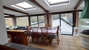 A dining area with a table and chairs, large windows, and a view of the outside. - Pleasant Holiday Home in Herbeumont near Semois River (Herbeumont)