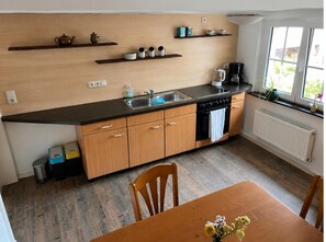 A compact kitchen with wooden cabinets, a black countertop, a sink, and a window with a view. - Ferienwohnung in Braunichswalde (Braunichswalde)
