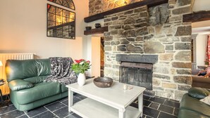Ett mysigt vardagsrum med en steneldstad, en grön lädersoffa, ett vitt soffbord och en dekorativ vas med blommor.