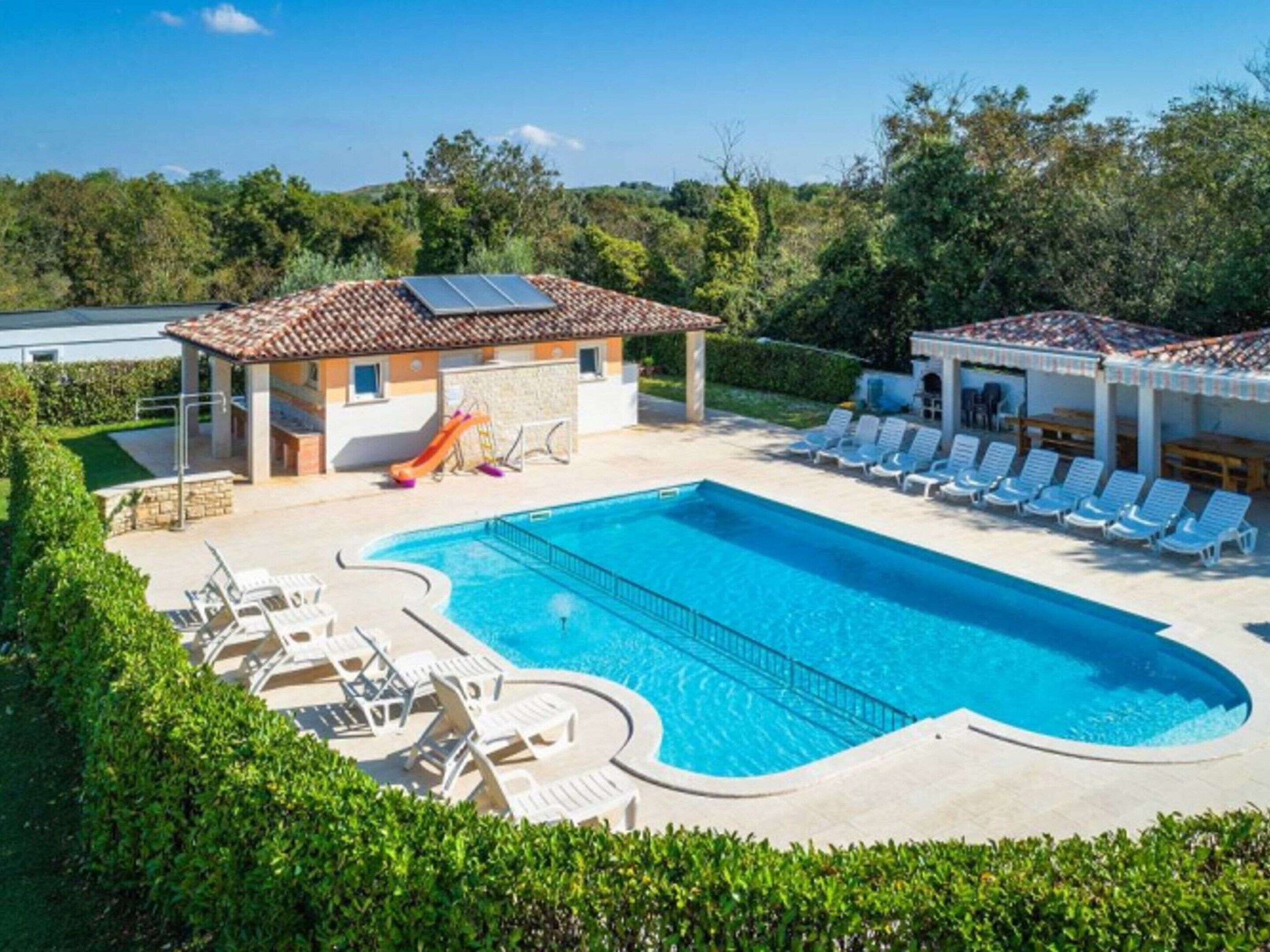 A swimming pool with lounge chairs, a slide, and a covered area with solar panels.