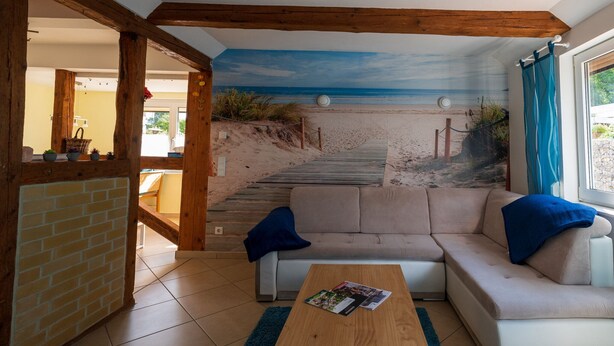 A living room with a sofa, a coffee table, and a mural of a beach scene. - Pleasant Apartment in Veckenstedt near Ilsenburg (Nordharz)