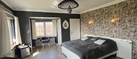 A bedroom with a large bed, a ceiling fan, a window with curtains, a radiator, and a wall-mounted light fixture.
