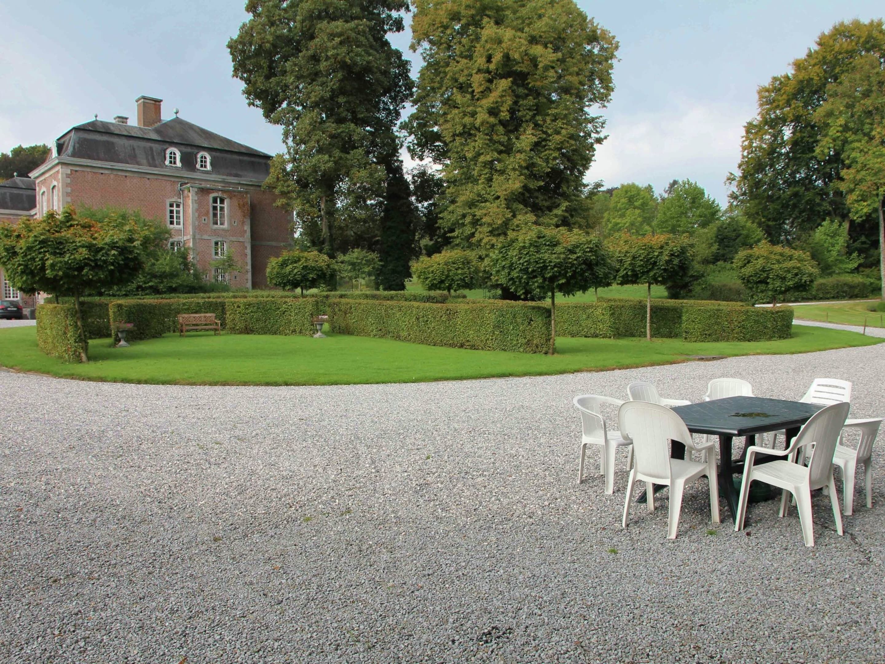 Eine Kiesterrasse mit Tisch und Stühlen, umgeben von einer gepflegten Hecke und Bäumen.