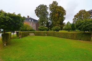 A well-maintained garden with a bench, neatly trimmed hedges, and a large tree.