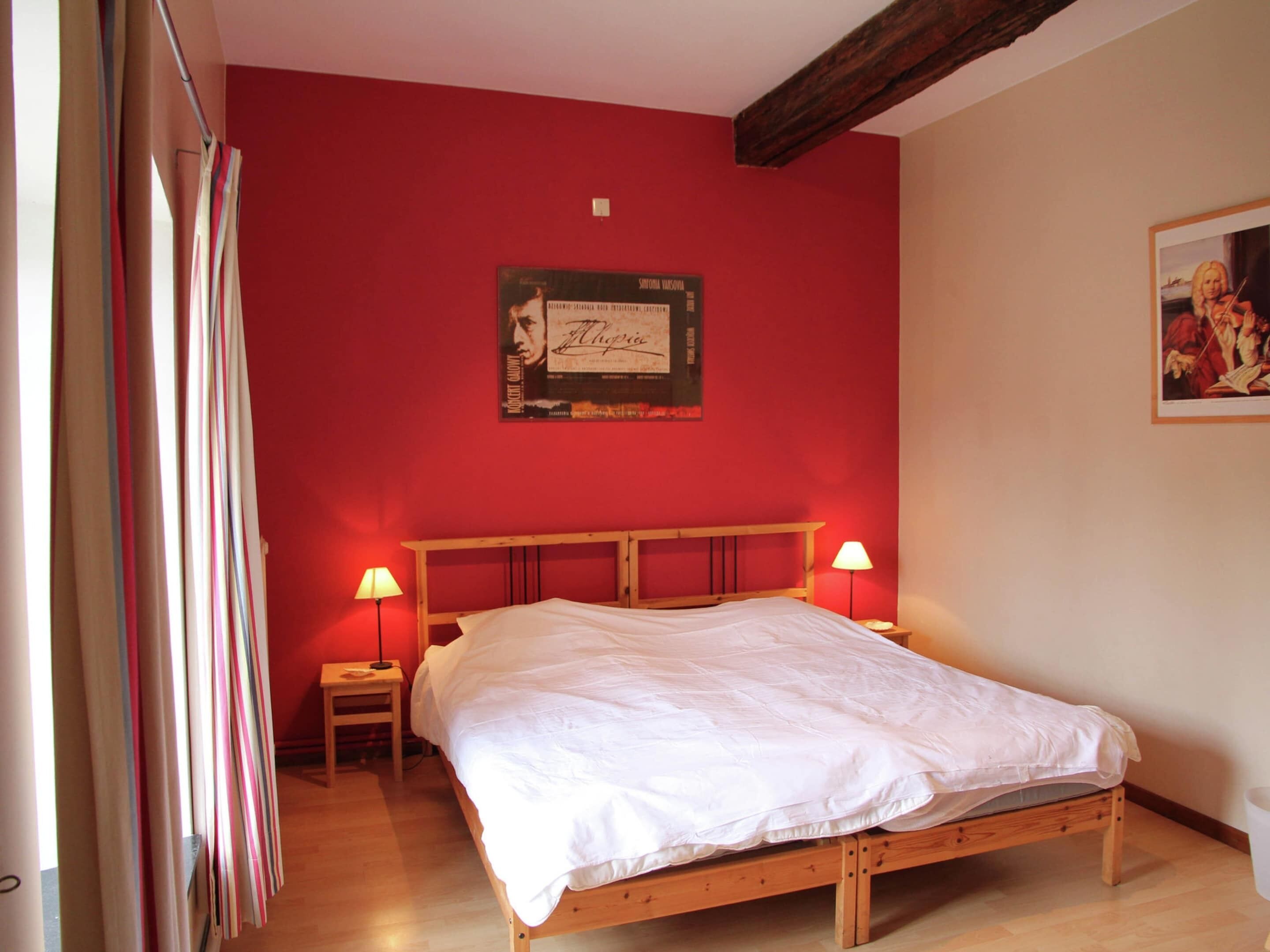 Une chambre à coucher avec un lit en bois, deux lampes de chevet, un mur rouge et une affiche encadrée au-dessus du lit.