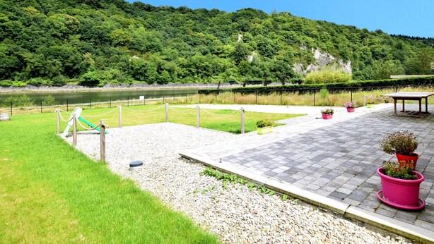 A riverside park with a paved walkway, seating areas, and potted plants. - Holiday Home in Hastiere Near Forest (Hastiere)