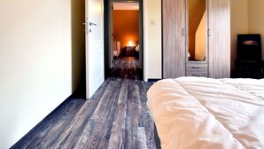 A hotel room with a wooden floor, a bed with white bedding, a wardrobe, and a desk with a chair. - Holiday Home in Hastiere Near Forest (Hastiere)