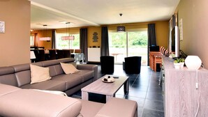 A modern living room with a sofa, coffee table, and dining area. There is a TV and a plant on the table. - Holiday Home in Hastiere Near Forest (Hastiere)