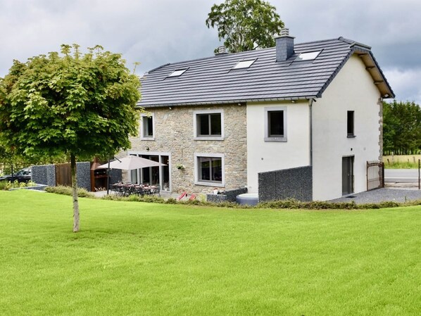 Ein modernes, zweistöckiges Haus mit Natursteinfassade, geneigtem Dach und gepflegtem Rasen.
