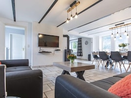 Una sala de estar moderna con un televisor de pantalla plana, un comedor con mesa y sillas, y una cocina visible al fondo.