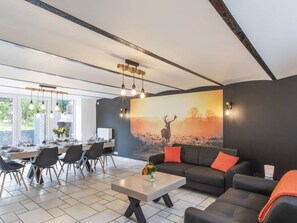 Ein modernes Wohnzimmer mit einem großen Hirschbild, einem dunkelgrauen Sofa und einem Essbereich mit Stühlen und einem Tisch.