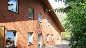 A red brick building with multiple windows, a satellite dish, and potted plants on the ground floor. - Cozy Apartment With Pool & Forest (Kirchdorf)